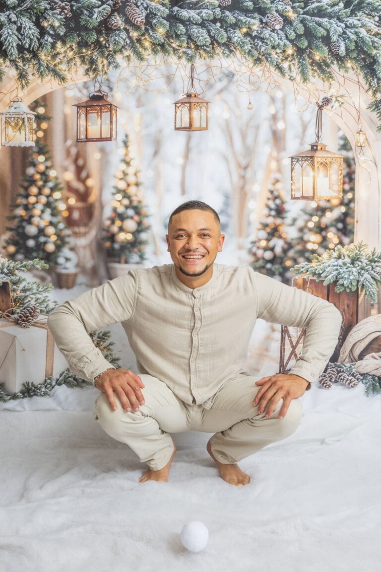 Homme souriant en tenue beige, séance photo de Noël avec décorations hivernales.