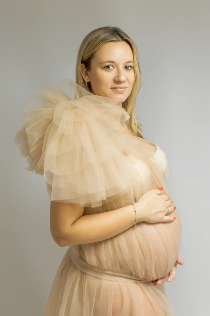 Femme enceinte en robe tulle beige, mains sur ventre