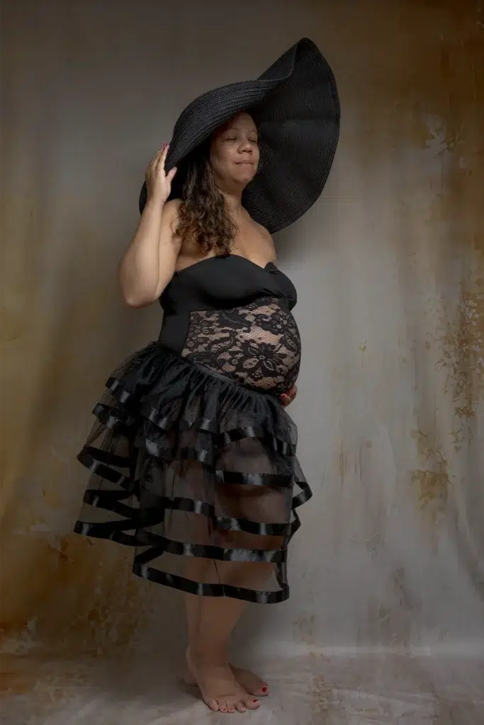 Femme enceinte en robe noire et grand chapeau – séance grossesse en studio à Ancenis
