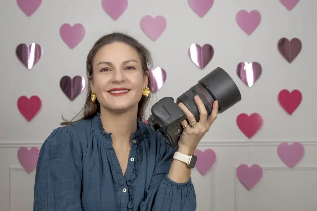 Photographe souriante tenant un appareil devant des cœurs roses